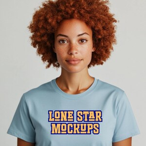 May include: A light blue t-shirt with the text "LONE STAR MOCKUPS" in a bold, two-tone design. The model has curly auburn hair and is looking directly at the camera. The shirt is a crew neck style.