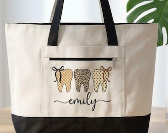May include: A beige tote bag with black handles and a black bottom. The front pocket features three decorated tooth graphics and the name "emily" in cursive. The word "Black" is in a white box in the lower left corner.