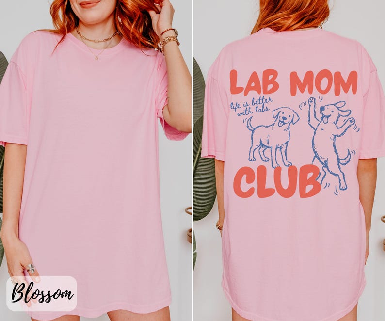 Puede incluir: Una camiseta rosa claro con el texto "LAB MOM CLUB" en coral y azul. La parte trasera de la camiseta presenta dos dibujos animados de perros labradores. La parte delantera de la camiseta tiene la palabra "Blossom" en cursiva.