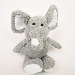 May include: A grey plush elephant toy with large ears, a white trunk, and white accents on the ears and feet. The elephant has black eyes and is sitting upright. This soft toy is suitable for children.