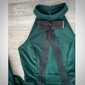 Könnte beinhalten: Dunkelgrünes Neckholder-Kleid mit hohem Kragen und schwarzer Spitzenschleife. Das Kleid hat ein figurbetontes Oberteil und einen fließenden Rock. Der Text "WHITE CAT Art Co" ist sichtbar.