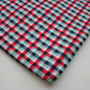 May include: A folded piece of fabric with a classic plaid pattern. The design features a grid of red, black, white, and light green squares. The fabric is likely cotton or a similar material, suitable for various sewing projects.