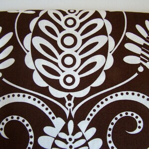 May include: Brown fabric with a white paisley pattern. The pattern features swirls, leaves, and circles.