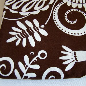 May include: Brown fabric with a white floral pattern. The pattern features swirls, leaves, and flowers.