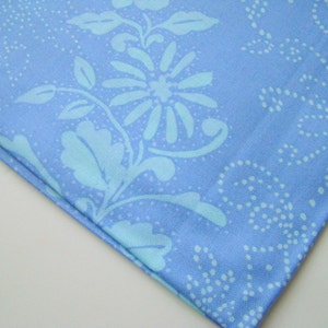 May include: A close-up of a light blue fabric with a white floral pattern. The fabric has a subtle texture and a soft, flowing feel.