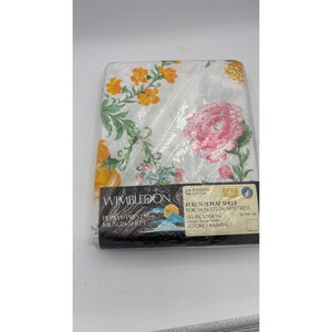 Könnte beinhalten: Ein weißes Betttuch in Kunststoffverpackung mit Blumenmuster, bestehend aus großen rosa Pfingstrosen und orangefarbenen Blüten mit grünen Blättern. Das Etikett zeigt Wimbledon Perma-Prest Muslin Sheet, für 137 cm x 190 cm Matratzen, 206 cm x 264 cm.