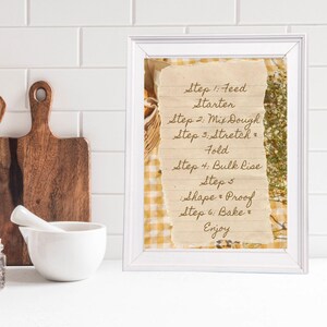 May include: A framed print with a white border displays handwritten steps for baking bread. The text on the aged paper reads "Feed Starter," "Mix Dough," "Stretch & Fold," "Bulk Lise," "Shape & Proof," "Bake & Enjoy."