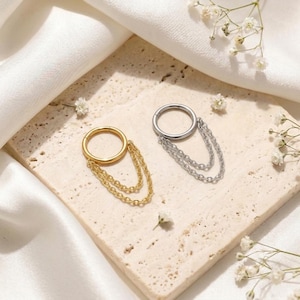 May include: Two hoop earrings, one gold-toned and one silver-toned, each featuring a hinged circular hoop connected to two delicate, dangling chain strands that drape from the bottom of the hoop, creating a layered and textured appearance.