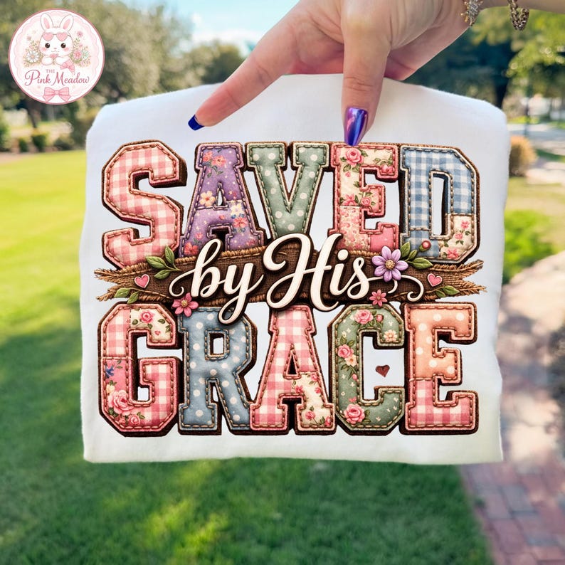 May include: White t-shirt with the phrase "SAVED by His GRACE" in a patchwork design. The letters use gingham and floral patterns, with floral accents. The shirt is held up by a hand. The design is in a feminine style.