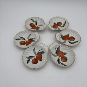 May include: Set of six white seashell-shaped dishes. Each dish features a hand-painted design of oranges and green leaves. The rims are trimmed with gold. These decorative dishes are ideal for serving small portions.