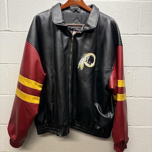 May include: Black leather jacket with burgundy sleeves and gold stripes. Features a team logo patch on the chest. The jacket has a full zipper closure and is hanging on a wooden hanger.