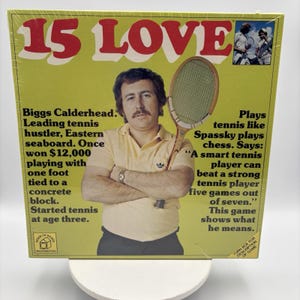May include: A square board game box titled 15 LOVE with a yellow background. The cover features a man in a yellow polo shirt holding a wooden tennis racket. Text details the character Biggs Calderhead, his tennis history, and game quotes.
