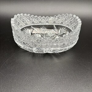 May include: A clear, oval-shaped crystal bowl featuring an intricate cut-glass pattern along the rim and a starburst design etched into the base. The sides display a textured diamond and cross-hatch motif that catches the light.