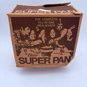 May include: A vintage Oster Super Pan box in brown with the text "THE COMPLETE ALL-IN-ONE MEALMAKER." The box features a graphic of people gathered around a table. The brand name "Oster" is prominently displayed.