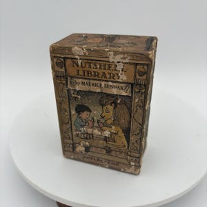 May include: A vintage "Nutshell Library" book by Maurice Sendak. The book has a brown cover with illustrations of a boy and a lion reading. The title is in a decorative font. The book is on a white surface.