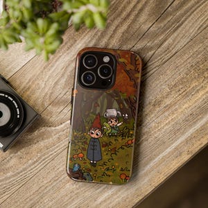 Könnte beinhalten: Eine Handyhülle mit einem Cartoon-Waldmotiv, das zwei Charaktere zeigt. Die Hülle hat ein braunes und oranges Farbschema und eine glänzende Oberfläche. Die Handyhülle liegt auf einer Holzoberfläche.