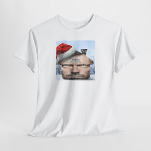 Puede incluir: Camiseta blanca con un gráfico de la cara de un hombre, integrado en un diseño de casa, con un gorro de Papá Noel. La palabra "Autismo" está impresa encima de la cara. El diseño está sobre un fondo nevado.