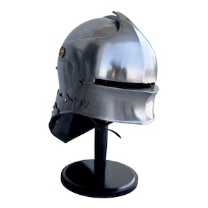 May include: A polished silver-colored metal helmet with a rounded dome, a horizontal visor slit, and a flared neck guard. The side features a small circular brass-toned emblem and the letters PZ engraved on the lower cheek section of the helmet.