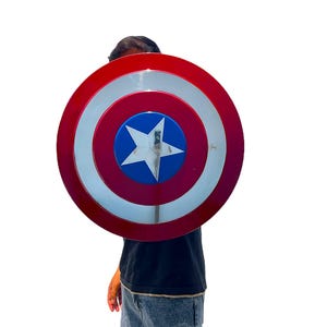 May include: A red, white, and blue Captain America shield. The shield has a red outer ring, a white inner ring, and a blue center with a white star. The shield is a circular shape.