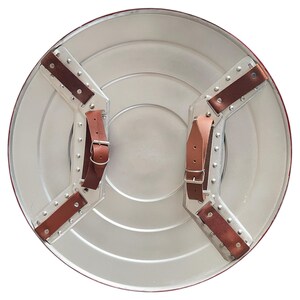 May include: A silver-colored, round shield with a red border. The back features brown leather straps and metal hardware for securing the shield. The shield has a classic, superhero-inspired design.