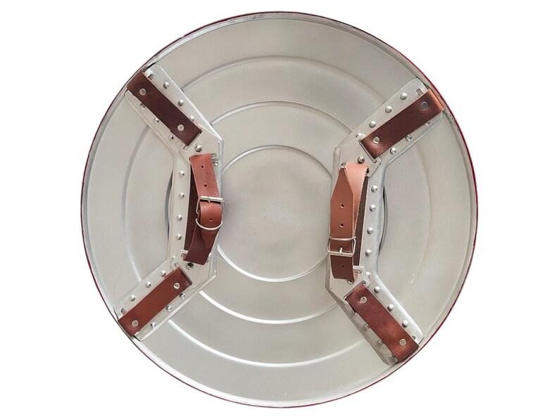 May include: A silver-colored, round shield with a red border. The back features brown leather straps and metal hardware for securing the shield. The shield has a classic, superhero-inspired design.