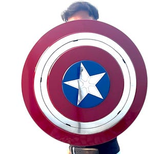 Peut inclure: Un bouclier Captain America rouge, blanc et bleu. Le bouclier est circulaire, avec une &eacute;toile blanche au centre d'un cercle bleu. L'anneau ext&eacute;rieur est rouge avec une bande argent&eacute;e.
