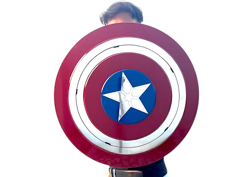 Peut inclure: Un bouclier Captain America rouge, blanc et bleu. Le bouclier est circulaire, avec une &eacute;toile blanche au centre d'un cercle bleu. L'anneau ext&eacute;rieur est rouge avec une bande argent&eacute;e.