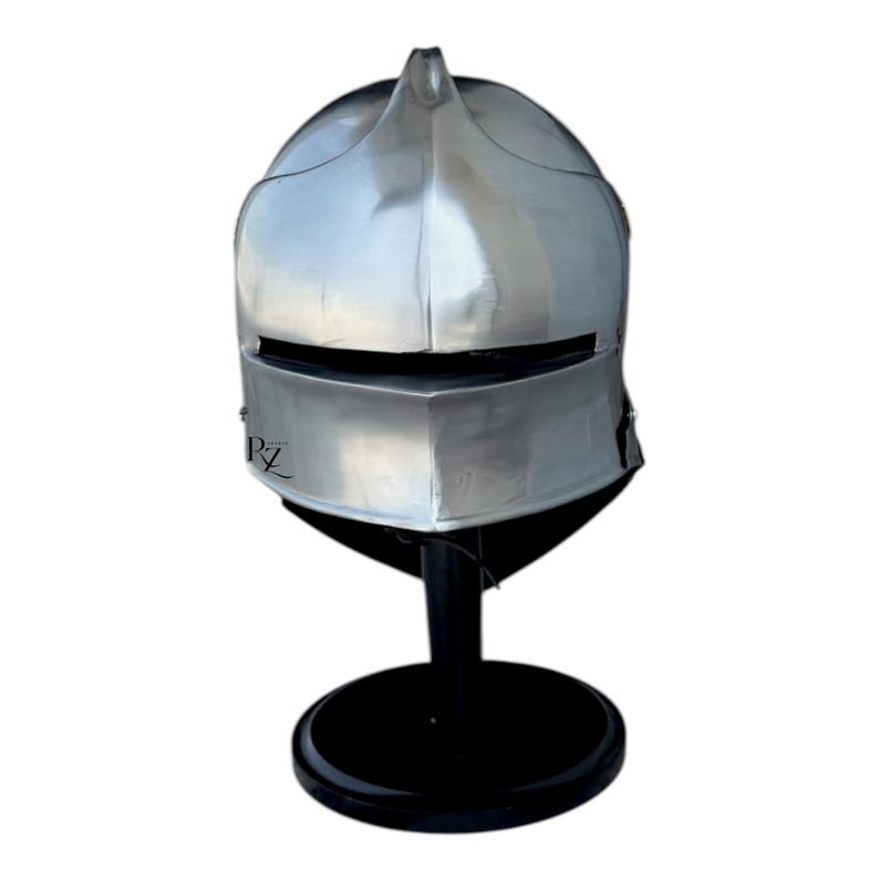 May include: A polished silver-colored metal helmet with a central ridge and a horizontal visor slit. The helmet features a smooth, rounded dome and a flared lower section. The letters RZ are printed in black on the lower left side of the visor.