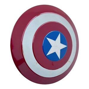 May include: A red, white, and blue shield with a star in the center. The shield is round with concentric circles of red, silver, and red. The center has a blue circle with a white star.