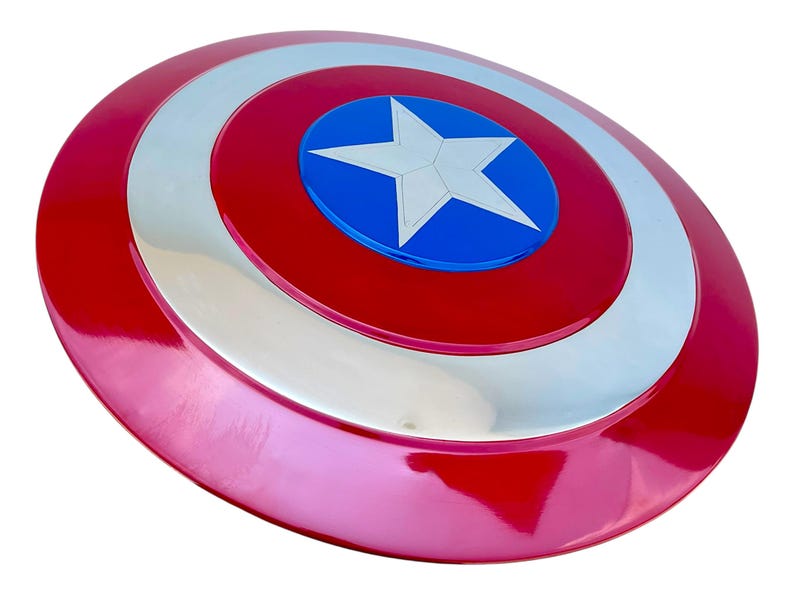 May include: A red, white, and blue shield with a central white star on a blue circle. The shield has a glossy finish and a circular design, reminiscent of a superhero's emblem.