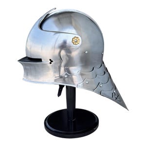 May include: A polished steel sallet helmet featuring a rounded dome, a narrow horizontal visor slit, and a multi-layered articulated neck guard. The helmet is accented with a small gold-toned floral rivet on the side and includes the letters RZ.