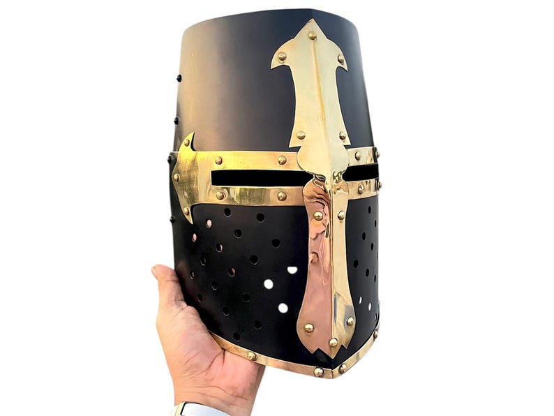 Pu&ograve; includere: Elmo medievale nero con croce e dettagli in ottone. L'elmo ha una parte superiore arrotondata ed &egrave; adornato da una prominente croce in ottone sul davanti. Sono visibili piccoli fori di ventilazione. Un pezzo storico o in costume.