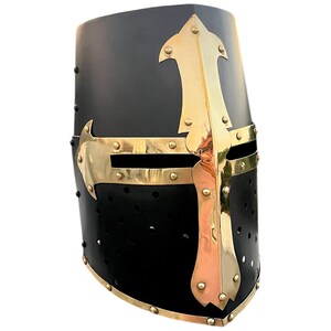 Pu&ograve; includere: Elmo medievale nero con dettagli in ottone. L'elmo presenta un design a croce e finiture in ottone. Sono visibili piccoli rivetti e fori per gli occhi. Un oggetto storico.