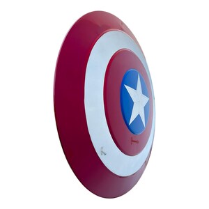 May include: A red, white, and blue shield with a star in the center. The shield has a circular design with a red outer ring, a white inner ring, and a blue center with a white star. The shield is a prop.