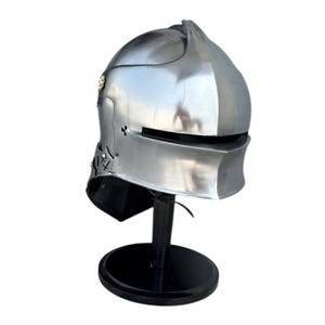 May include: A polished silver-colored metal knight helmet featuring a rounded dome, a horizontal eye slit, and a neck guard. The side of the helmet displays a small circular emblem and the black printed letters PZ. It is mounted on a black stand.