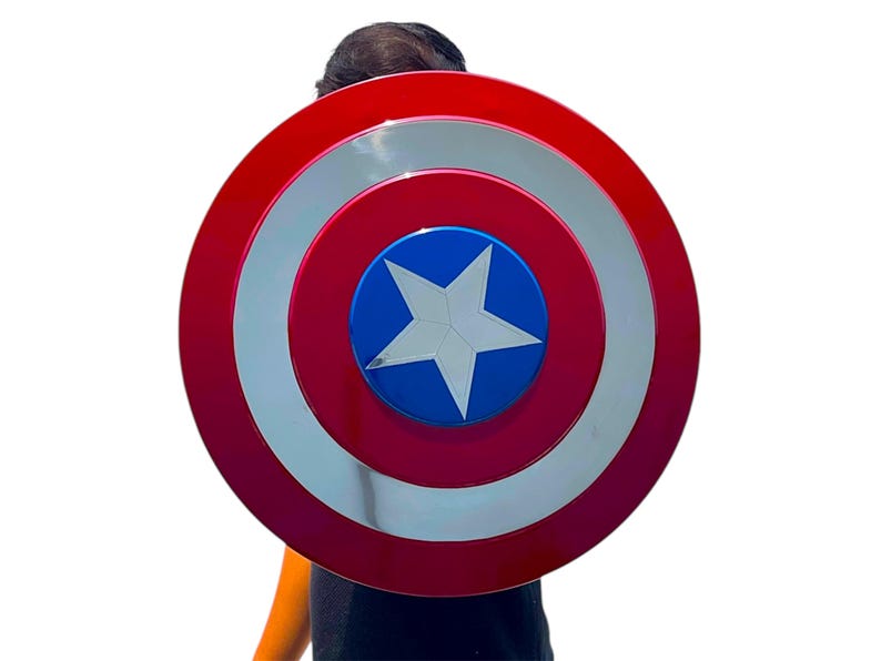 May include: A red, white, and blue shield with a star in the center. The shield has a circular design with concentric rings of red, silver, and red. The center is blue with a white star.