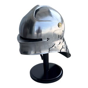 May include: A polished steel medieval-style helmet featuring a rounded dome, a visor with a horizontal eye slit, and a neck guard with scalloped edges. A small gold-colored floral rivet is visible on the side, along with the black text RZ.