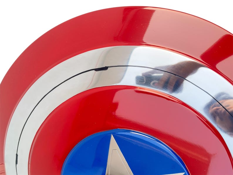Peut inclure: Gros plan sur un bouclier rouge, blanc et bleu avec un embl&egrave;me d'&eacute;toile. Le bouclier a une finition brillante et un design circulaire. Les couleurs du bouclier sont le rouge, le blanc et le bleu.