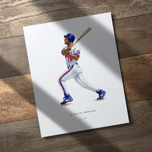May include: A print featuring a baseball player in a white and blue uniform, swinging a bat. The player is wearing a blue helmet and shoes. The print includes the text "Moises Alou // Montreal Expos".