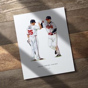May include: A print featuring two baseball players in white and red uniforms, fist-bumping. One player wears number 25. The print is on a white background with the text "Andrew Jones / Chipper Jones / Atlanta Braves".