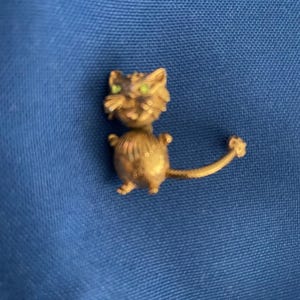 May include: A gold-colored metal cat figurine with green eyes. The cat is standing on all fours with its tail curled up behind it.