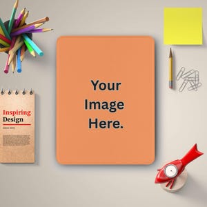 May include: An orange rectangular pad with rounded corners, featuring the text "Your Image Here." A notepad with "Inspiring Design" is on the left. Pencils, a yellow sticky note, paper clips, and a red rocket-shaped object are also visible.