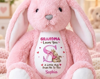 May include: A plush pink rabbit stuffed animal with long ears and a white belly patch. The patch features the text "GRANDMA Loves You", a large letter "S", an illustration of two bunnies, and the text "A Little Hug From Me To You" and "Sophia".