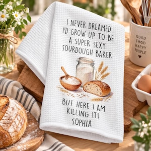 May include: A white waffle-weave kitchen towel featuring the black text I NEVER DREAMED I'D GROW UP TO BE A SUPER SEXY SOURDOUGH BAKER BUT HERE I AM KILLING IT! SOPHIA, with a graphic of a glass jar of flour, a wooden bowl, and bread.