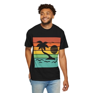 May include: Black t-shirt featuring a retro sunset design. The graphic includes a palm tree, sun, and birds against a backdrop of horizontal stripes in orange, yellow, green, and blue. A casual, comfortable tee.