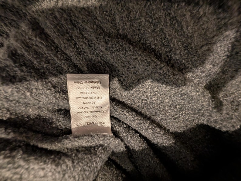 May include: Close-up of a gray knit fabric with a tag attached. The tag reads "Made in China" and lists fabric composition as 75% nylon and 25% rayon. The fabric has a soft, textured appearance.