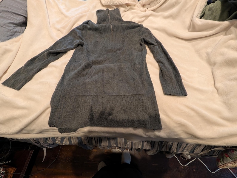May include: A gray, long-sleeved sweater dress with a high, zippered collar. The dress has a ribbed texture and a relaxed fit. The sleeves are long and the hemline falls below the hips. The dress is made of a soft, knit material.
