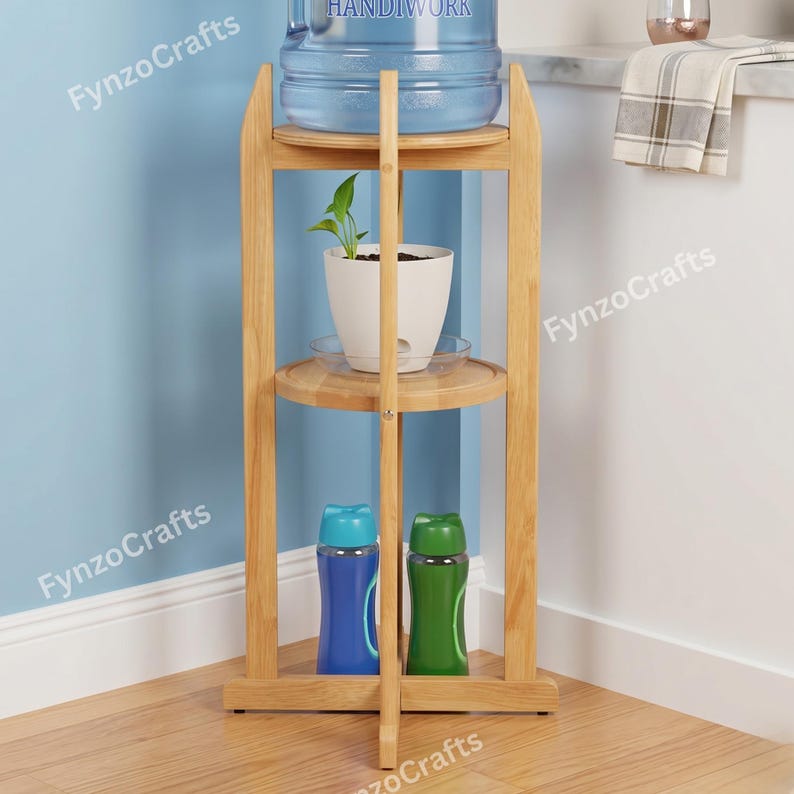 Pu&ograve; includere: Un supporto in legno per refrigeratore d'acqua con tre ripiani. Il ripiano superiore contiene una grande brocca d'acqua. Il ripiano centrale ha una pianta in vaso bianca. Il ripiano inferiore mostra una bottiglia d'acqua blu e verde. Il supporto &egrave; in legno chiaro.