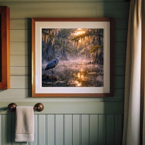 Poster | Louisiana Bayou Sunrise Print, Swamp Art, Southern Landscape, Nature Art, Tranquil Artwork

Step into the tranquil beauty of the Deep South with this atmospheric art print featuring a misty Louisiana swamp at sunrise. A majestic great blue heron stands poised on a mossy stump, its silhouette framed by golden light filtering through ancient cypress trees draped in Spanish moss. The still water mirrors the soft glow of dawn and scattered lily pads, creating a serene, dreamlike reflection.
