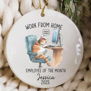 May include: White ceramic ornament with a cartoon cat working from home. The cat is wearing headphones and sitting in a blue chair in front of a computer. Text on the ornament reads "Work From Home", "Employee of the Month", and a name and year.
